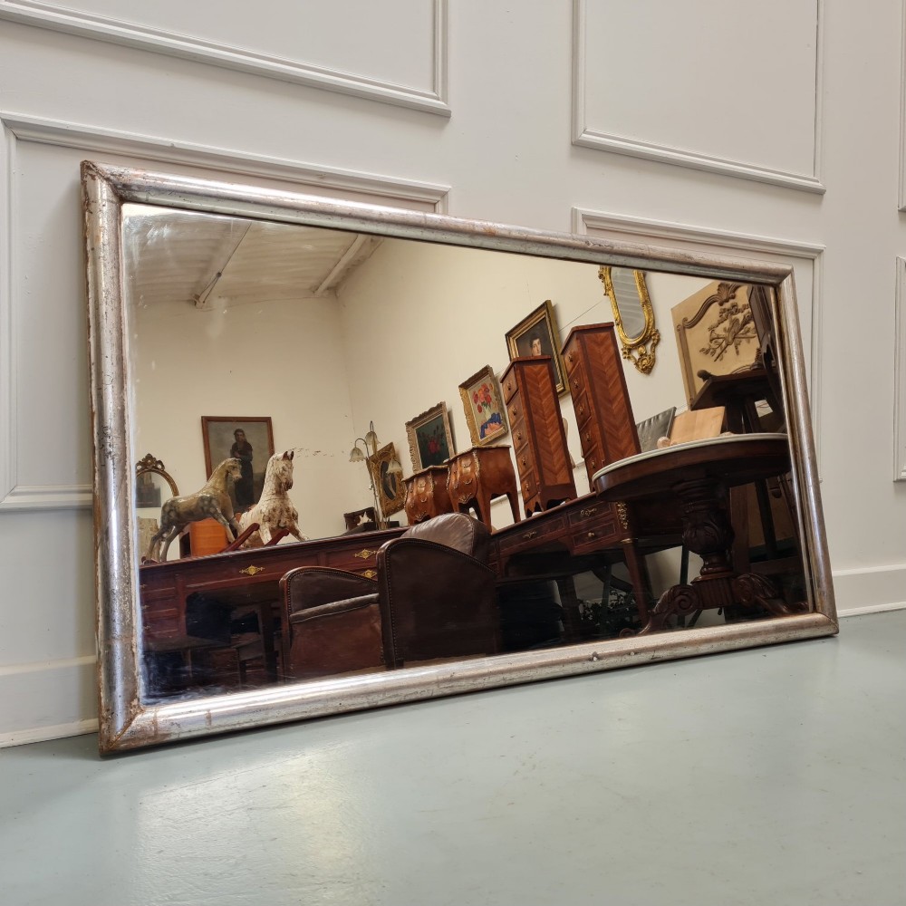 A large horizontal rectangular mirror featuring a simple moulded frame with a silver gilt finish and a reflective glass plate.