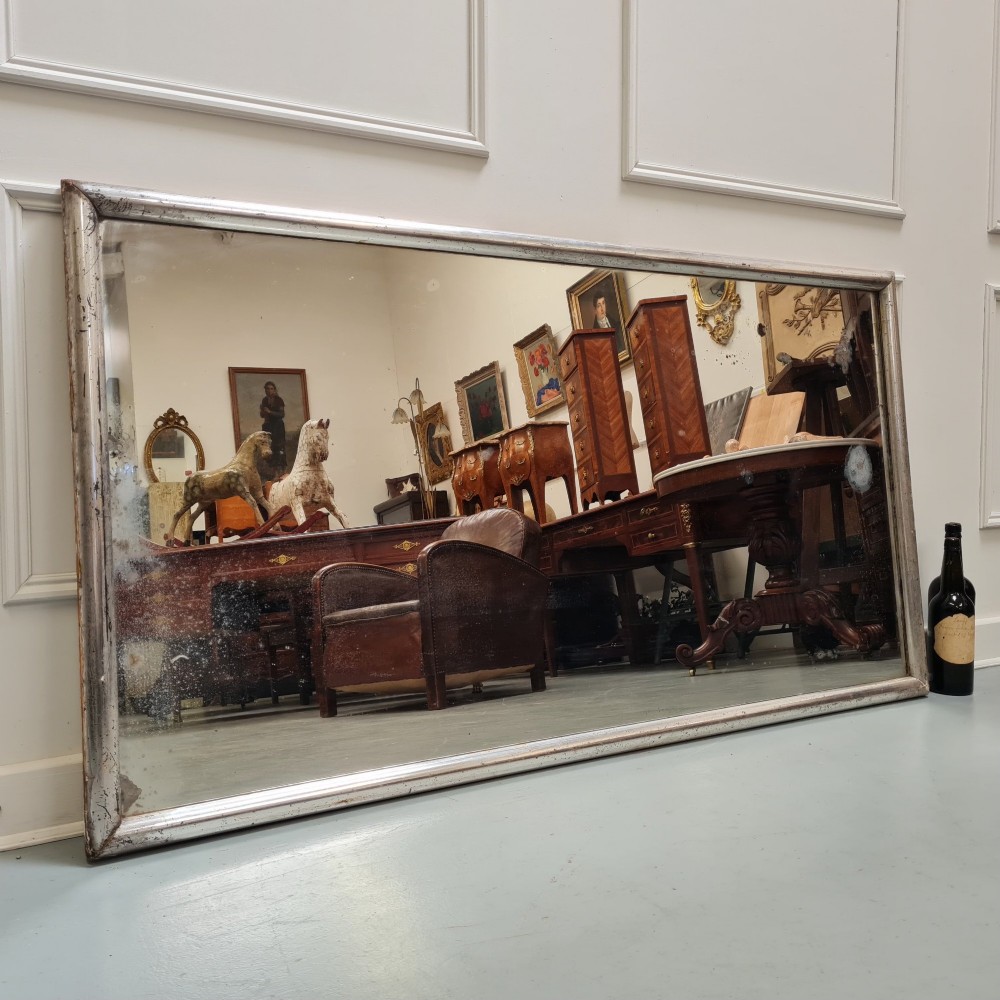 A large horizontal rectangular mirror featuring a simple moulded frame with a silver gilt finish and a reflective glass plate. View II