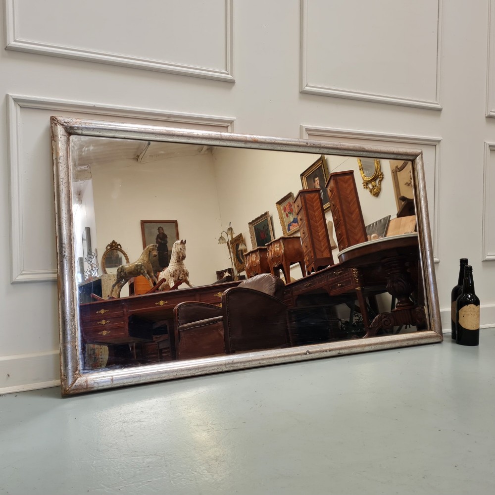 A large horizontal rectangular mirror featuring a simple moulded frame with a silver gilt finish and a reflective glass plate. View III