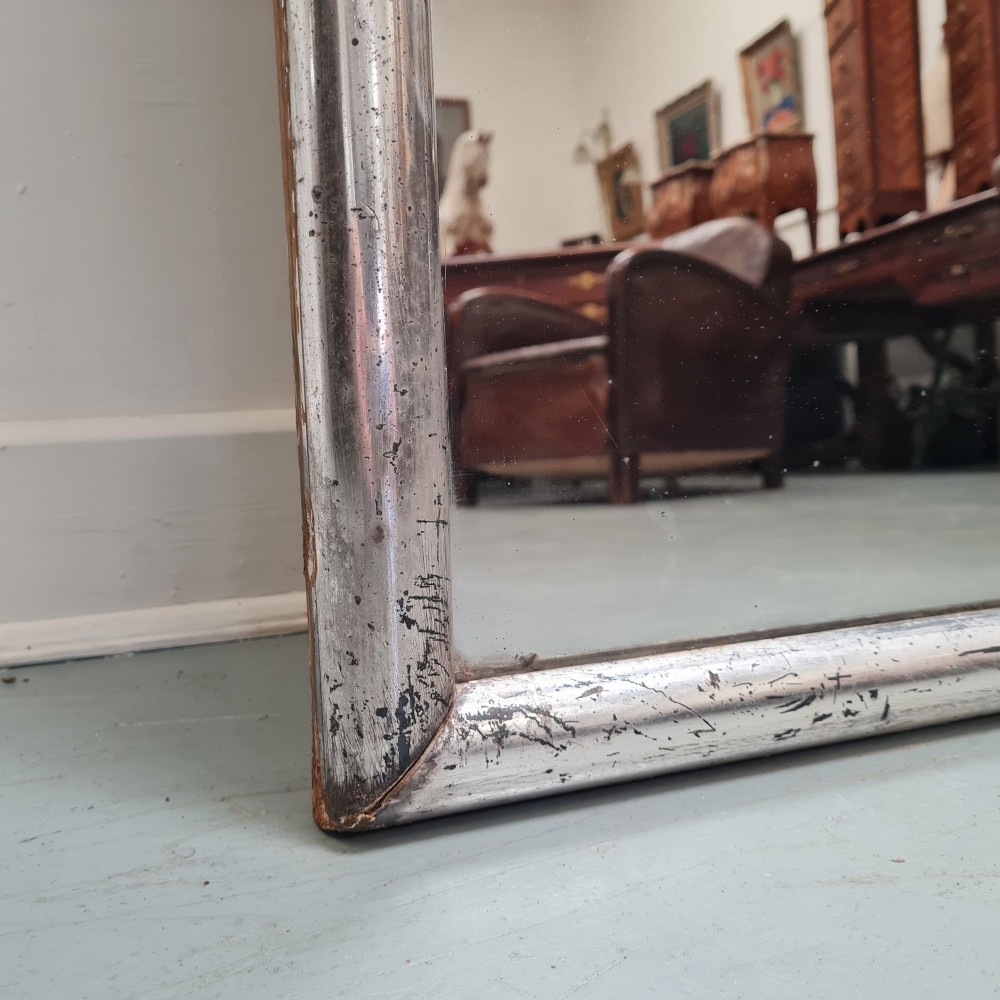 A large horizontal rectangular mirror featuring a simple moulded frame with a silver gilt finish and a reflective glass plate. View V