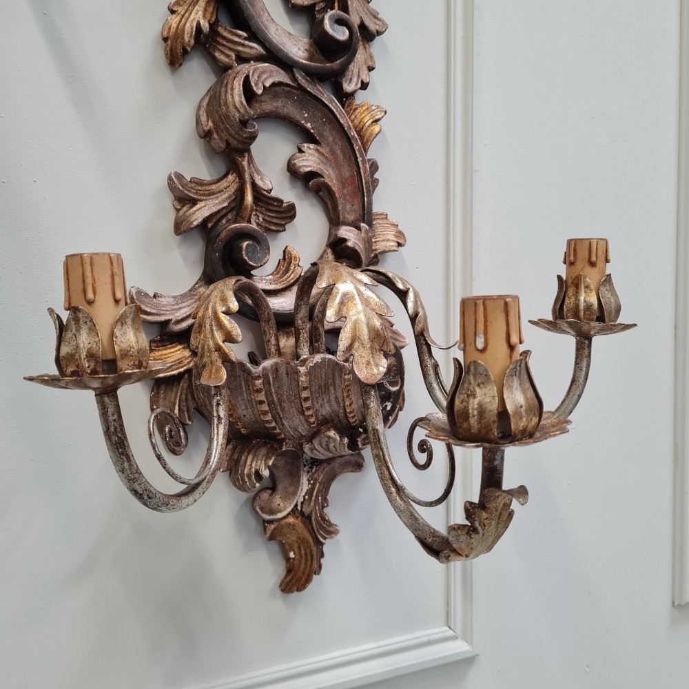 A pair of carved wooden Italian wall sconces featuring ornate acanthus leaf scrolls, gilded highlights, and three metal candle-style light branches. View IV