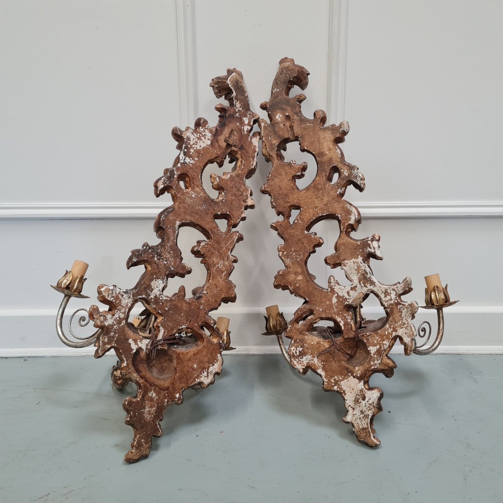 A pair of carved wooden Italian wall sconces featuring ornate acanthus leaf scrolls, gilded highlights, and three metal candle-style light branches. View V