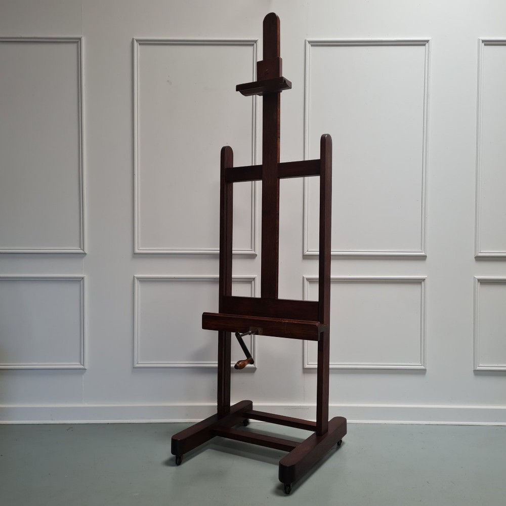 An antique dark oak studio winder easel featuring a mechanical hand crank handle and a floor base equipped with castors.