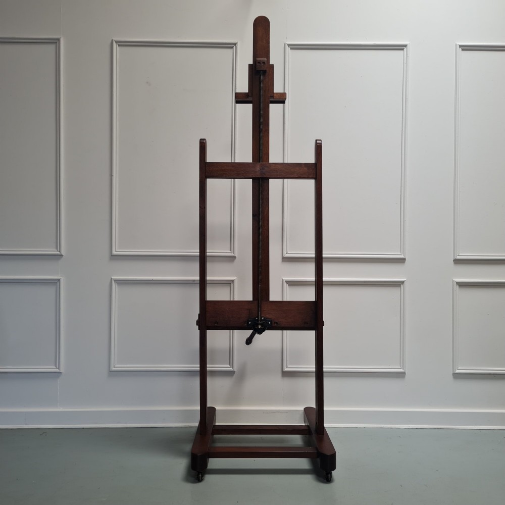 An antique dark oak studio winder easel featuring a mechanical hand crank handle and a floor base equipped with castors. View V