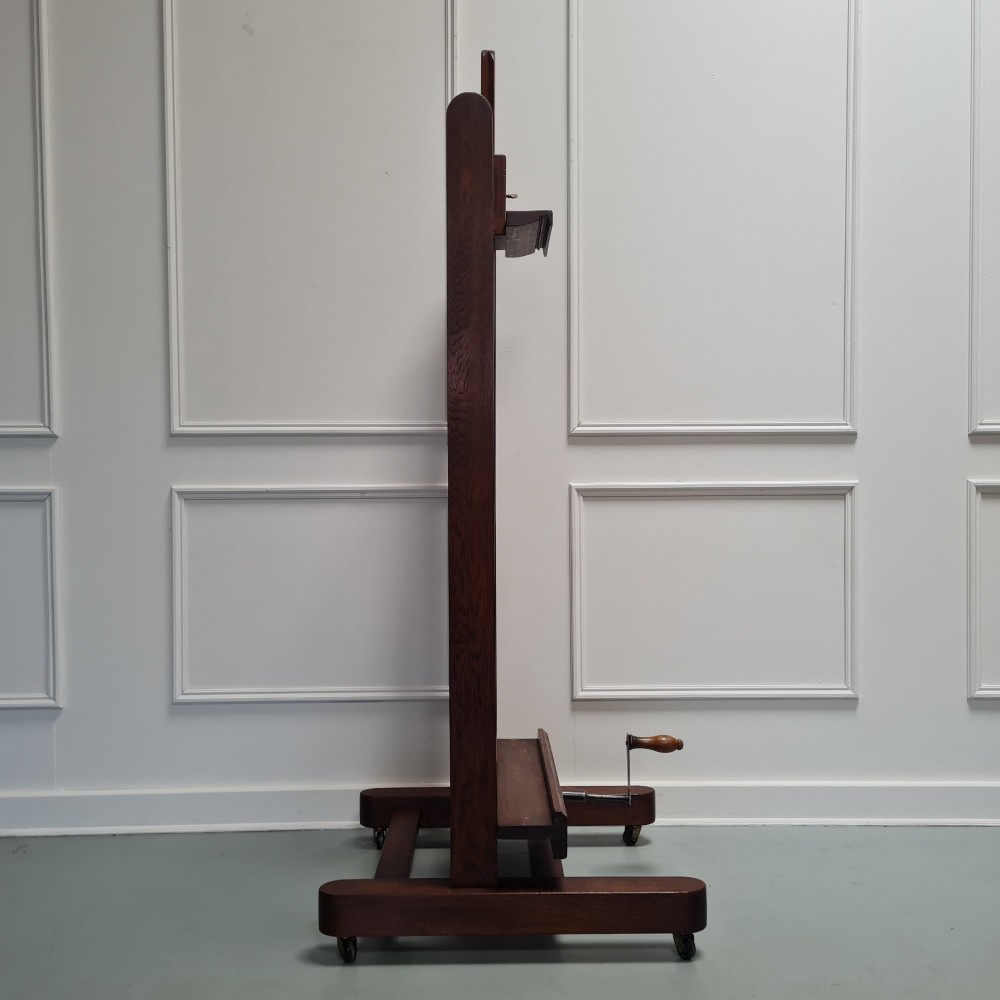 An antique dark oak studio winder easel featuring a mechanical hand crank handle and a floor base equipped with castors. View IX
