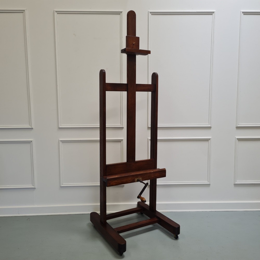 An antique dark oak studio winder easel featuring a mechanical hand crank handle and a floor base equipped with castors. View X
