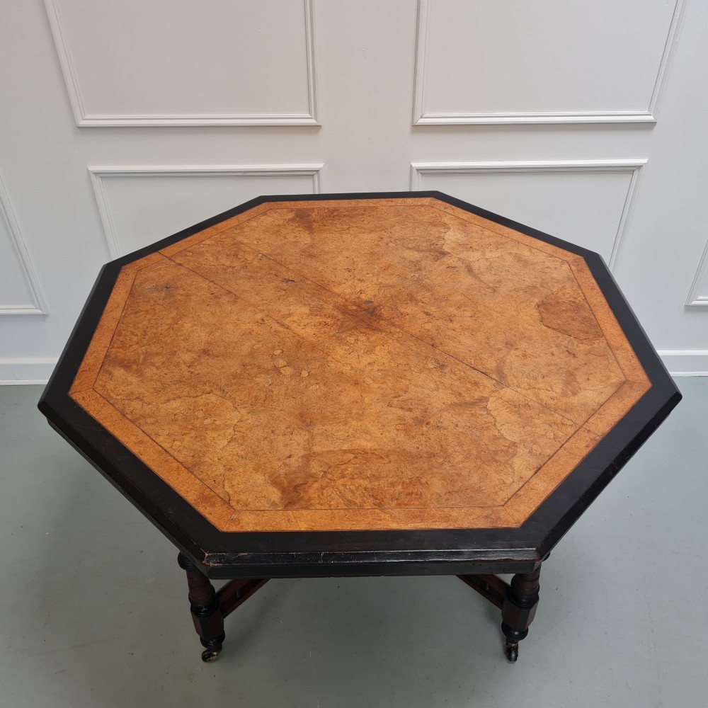 An octagonal Victorian Aesthetic Movement centre table featuring a light wood veneered top with ebonised borders, turned legs, and cross-stretchers with turned spindles. View II