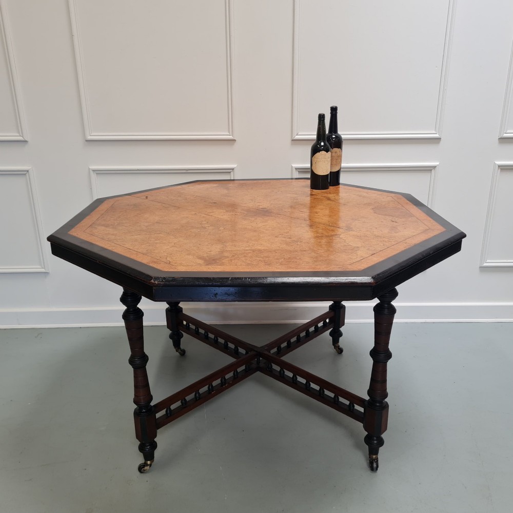 An octagonal Victorian Aesthetic Movement centre table featuring a light wood veneered top with ebonised borders, turned legs, and cross-stretchers with turned spindles. View III