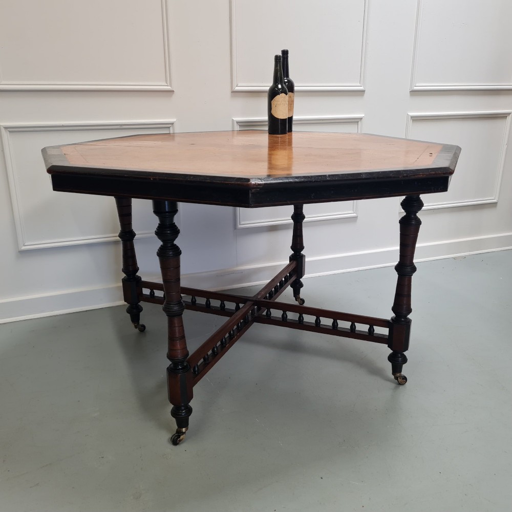 An octagonal Victorian Aesthetic Movement centre table featuring a light wood veneered top with ebonised borders, turned legs, and cross-stretchers with turned spindles. View V