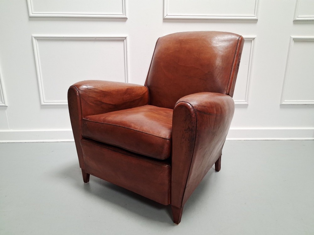 A 1930s French leather club chair upholstered in warm cognac brown patinated leather with rounded armrests and short square feet.