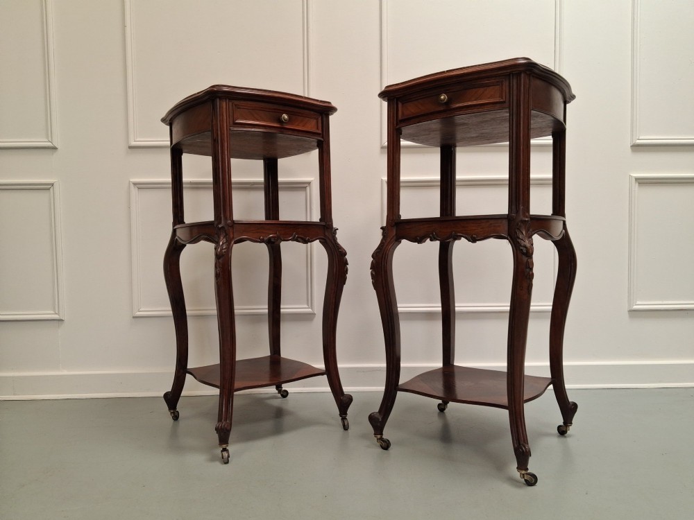 A matching pair of tall dark wood end tables featuring top drawers, lower open shelves, carved cabriole legs, and brass castors. View II