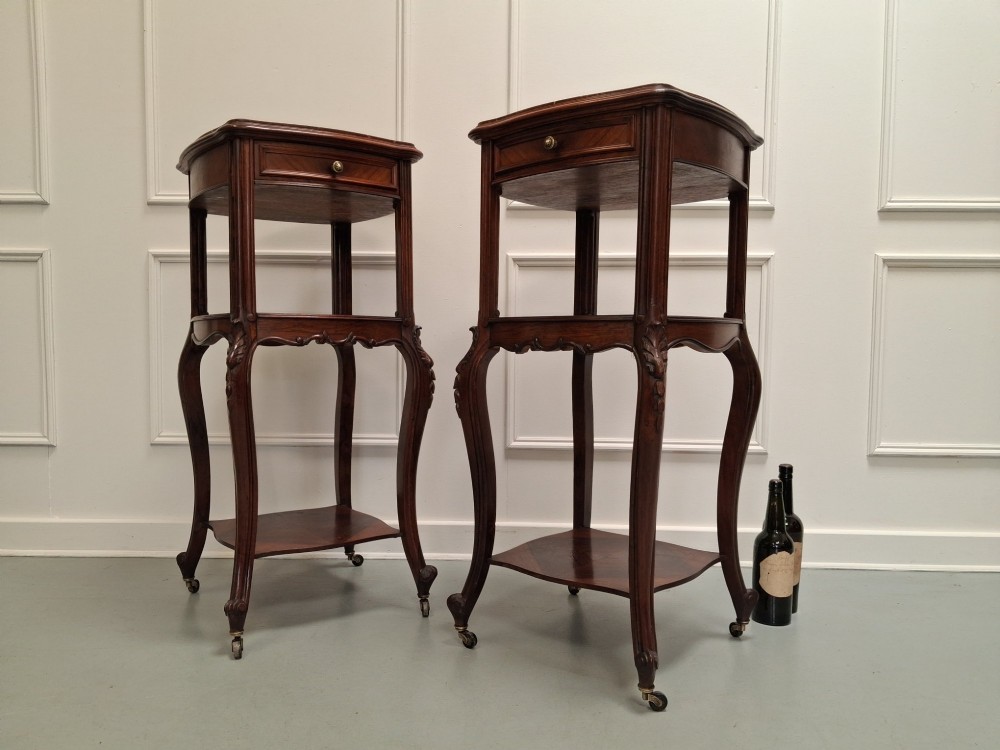 A matching pair of tall dark wood end tables featuring top drawers, lower open shelves, carved cabriole legs, and brass castors. View III