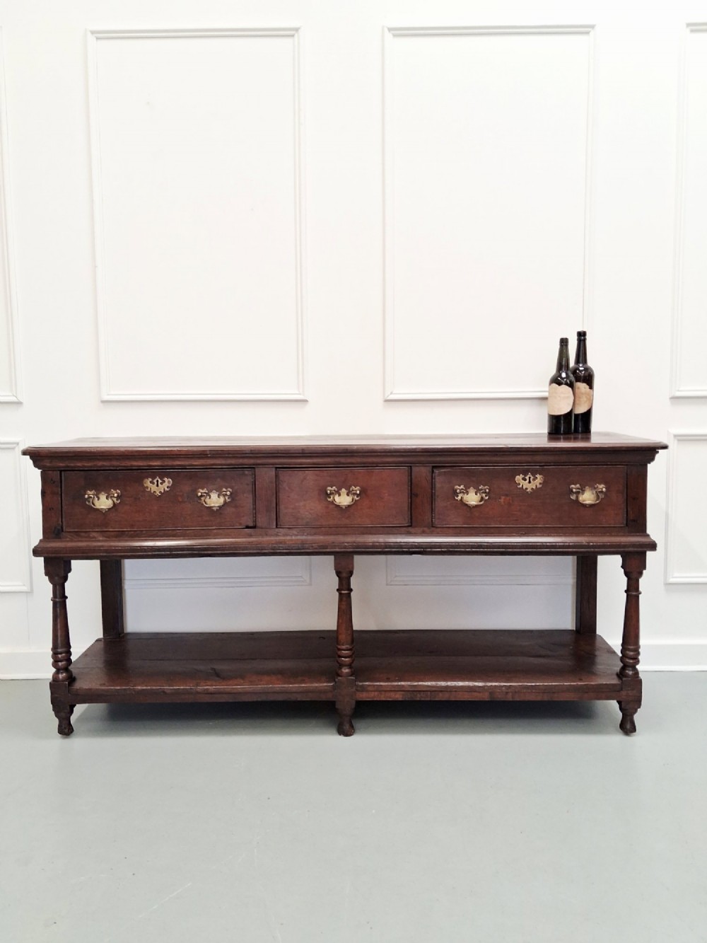 An 18th-century dark oak Georgian dresser base featuring three drawers with brass handles, turned front legs, and a low pot board shelf. View III