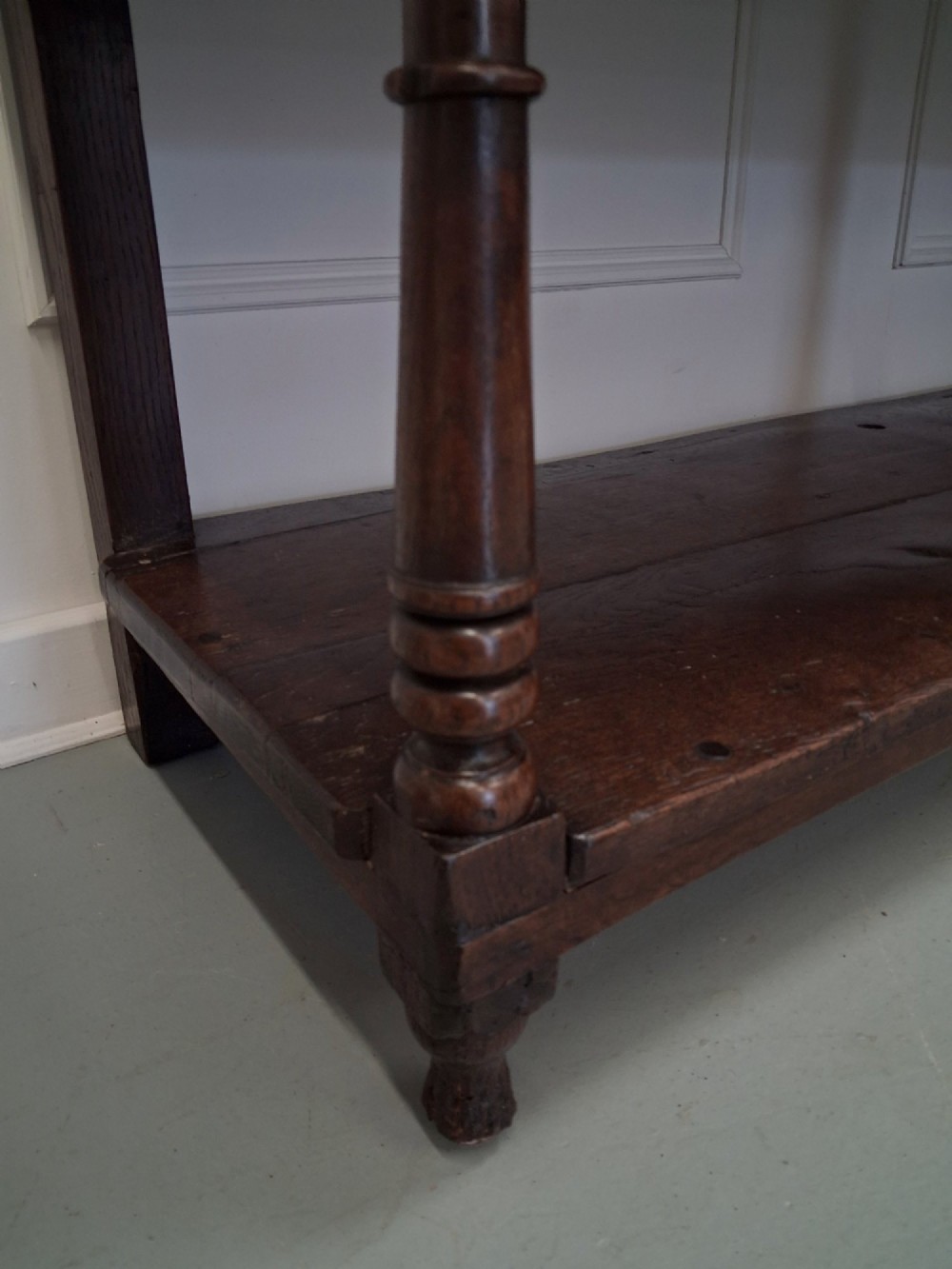An 18th-century dark oak Georgian dresser base featuring three drawers with brass handles, turned front legs, and a low pot board shelf. View V