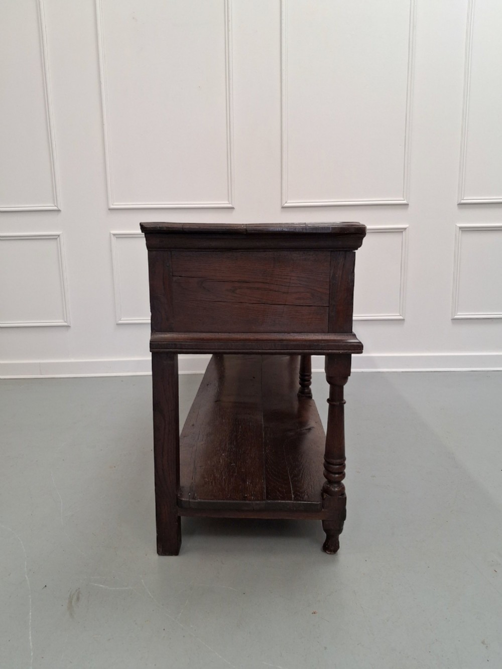 An 18th-century dark oak Georgian dresser base featuring three drawers with brass handles, turned front legs, and a low pot board shelf. View IX