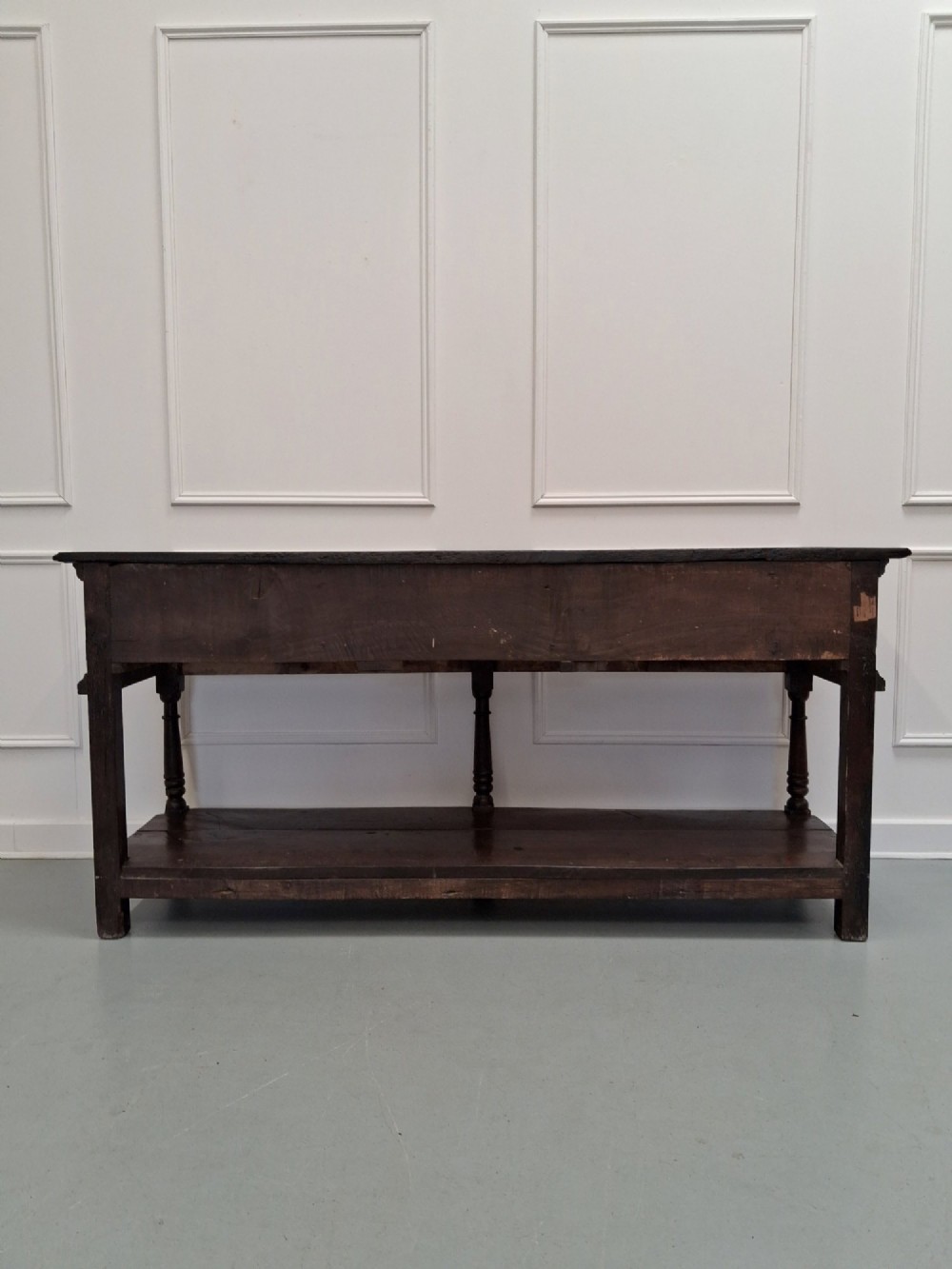 An 18th-century dark oak Georgian dresser base featuring three drawers with brass handles, turned front legs, and a low pot board shelf. View X