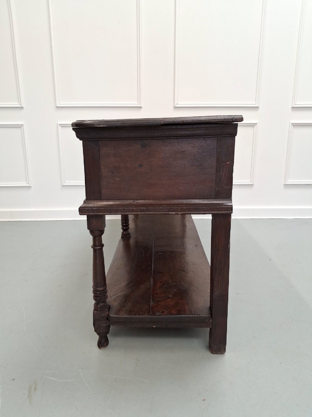 An 18th-century dark oak Georgian dresser base featuring three drawers with brass handles, turned front legs, and a low pot board shelf. View XI