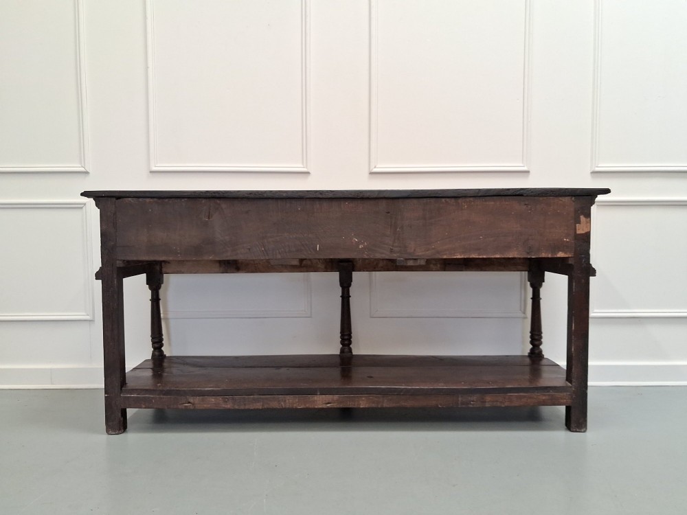 An 18th-century dark oak Georgian dresser base featuring three drawers with brass handles, turned front legs, and a low pot board shelf. View XII