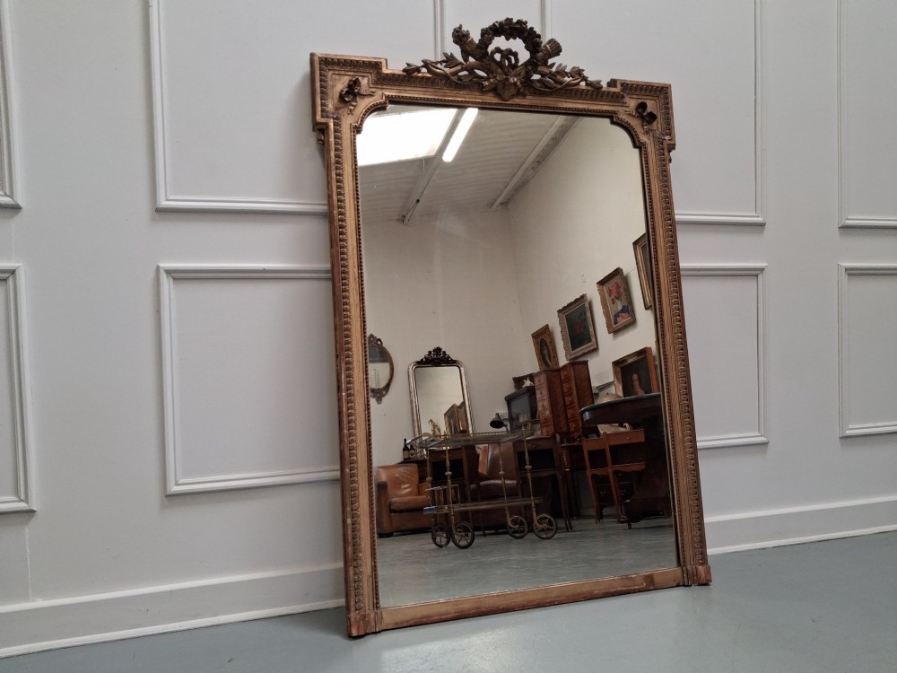 Large 19th-century French giltwood mirror with a carved crest pediment and beaded inner frame.