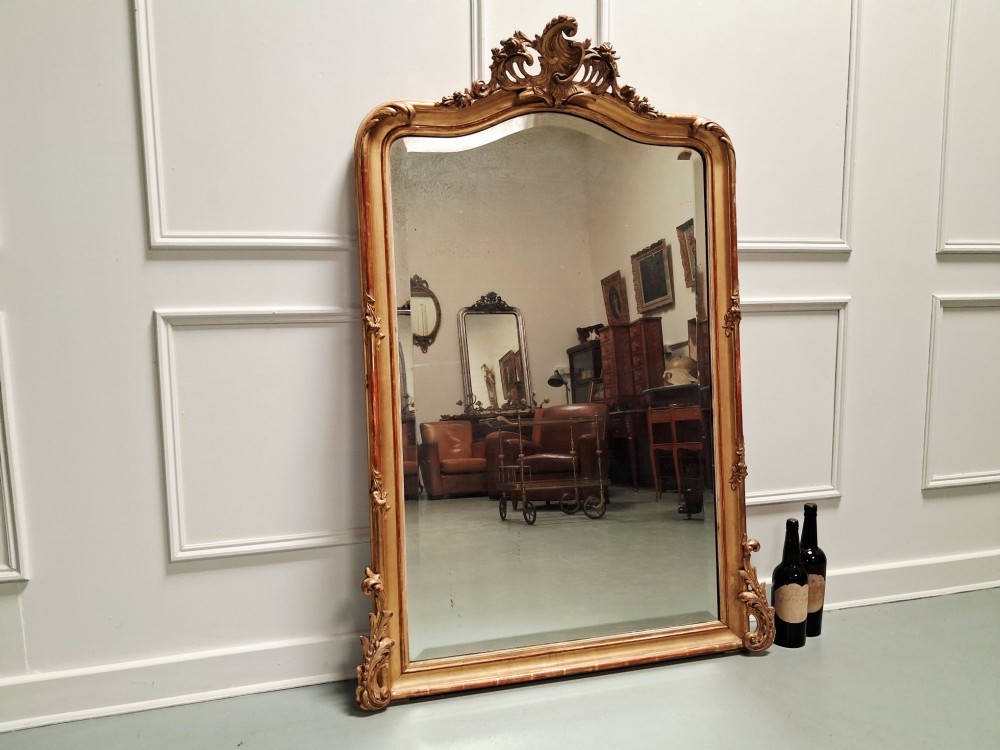 A large nineteenth-century French Rococo giltwood wall mirror with an arched top crested by an ornate shell and scroll carving. View II