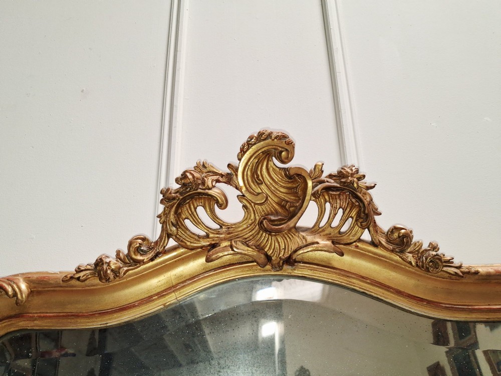 A large nineteenth-century French Rococo giltwood wall mirror with an arched top crested by an ornate shell and scroll carving. View VI