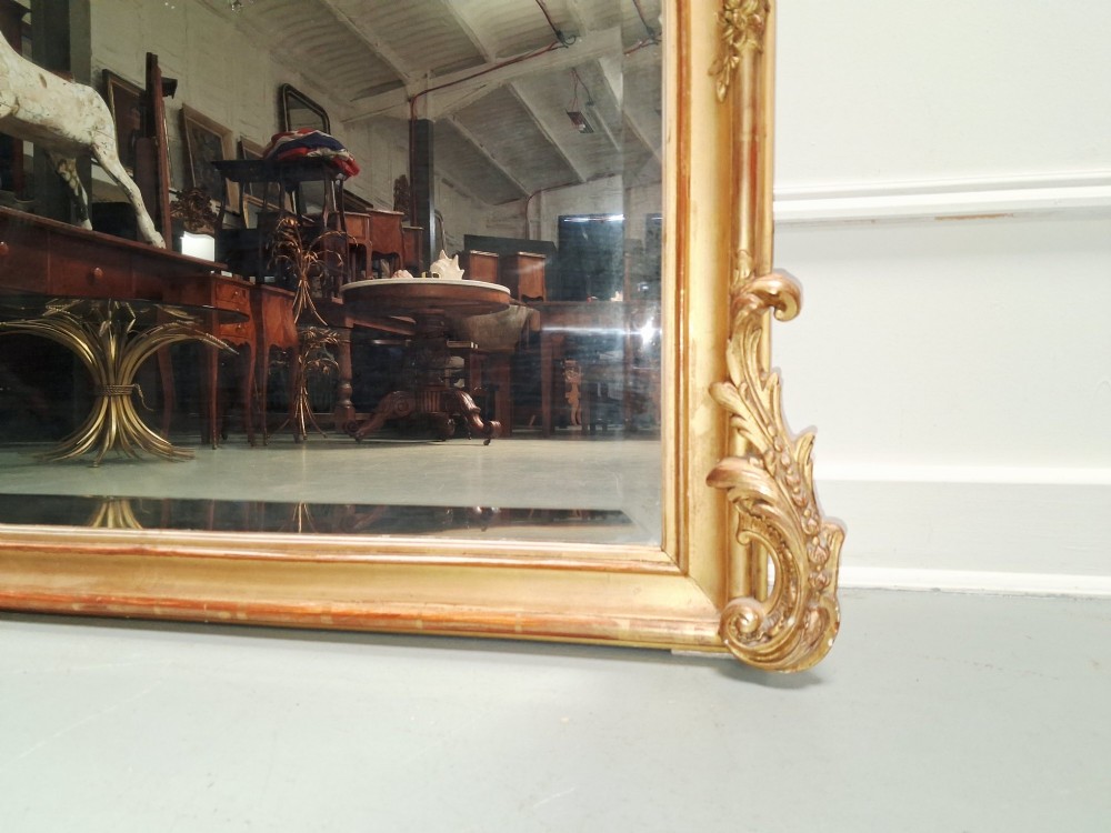 A large nineteenth-century French Rococo giltwood wall mirror with an arched top crested by an ornate shell and scroll carving. View VII