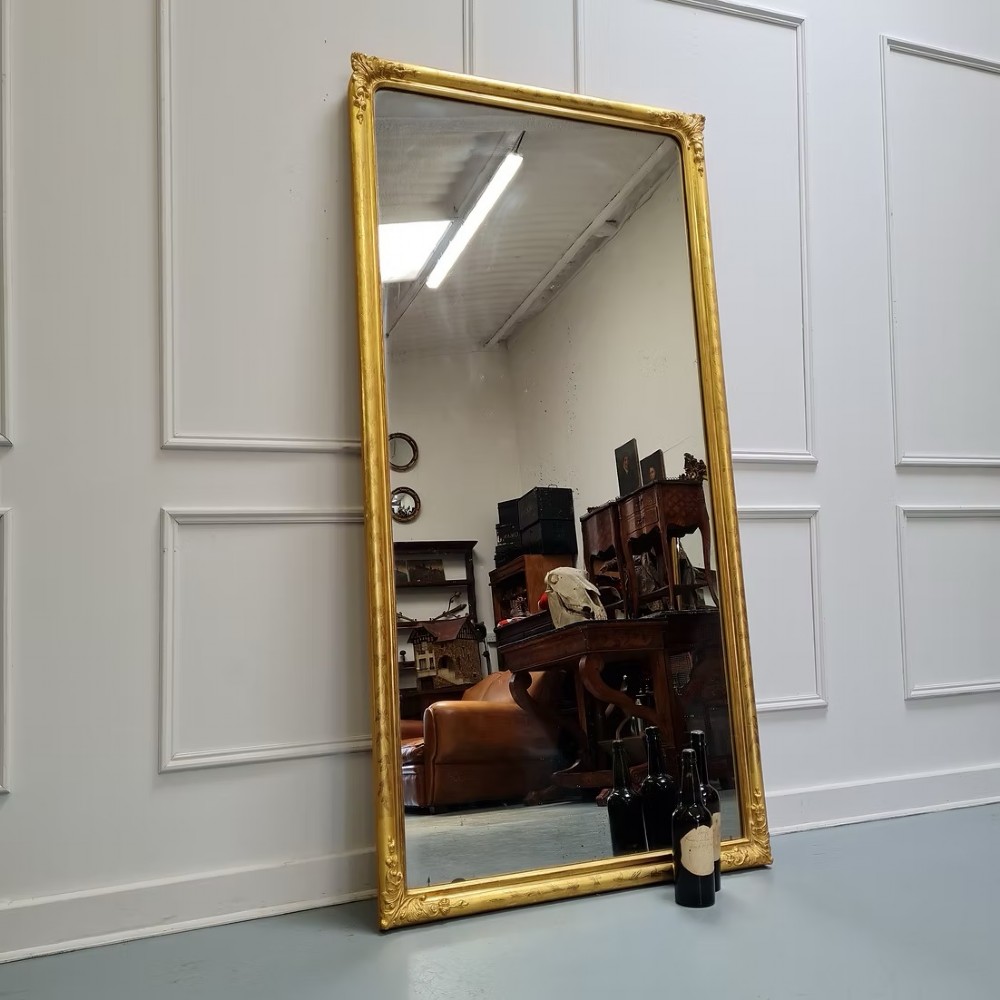 A tall rectangular French antique floor mirror featuring a gold gilded frame with rounded top corners and leaf details.