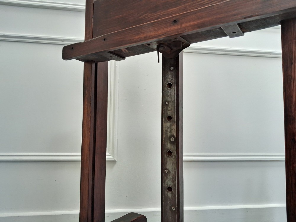 A tall dark pitch pine studio easel featuring an adjustable central mast, lower support shelf, and base castors. View IV