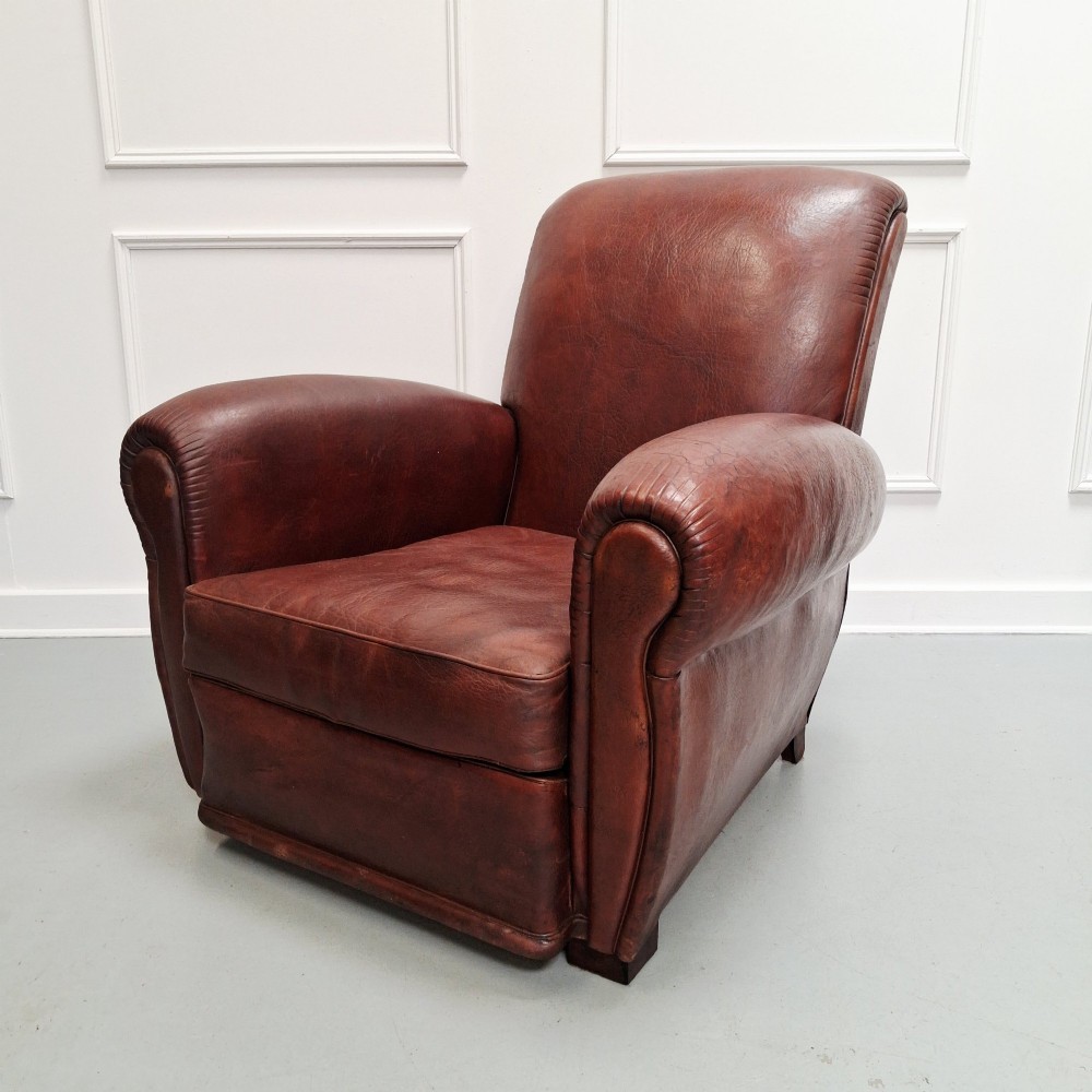 A French Art Deco club armchair upholstered in patinated brown leather with rolled arms, a high backrest, and low square feet.