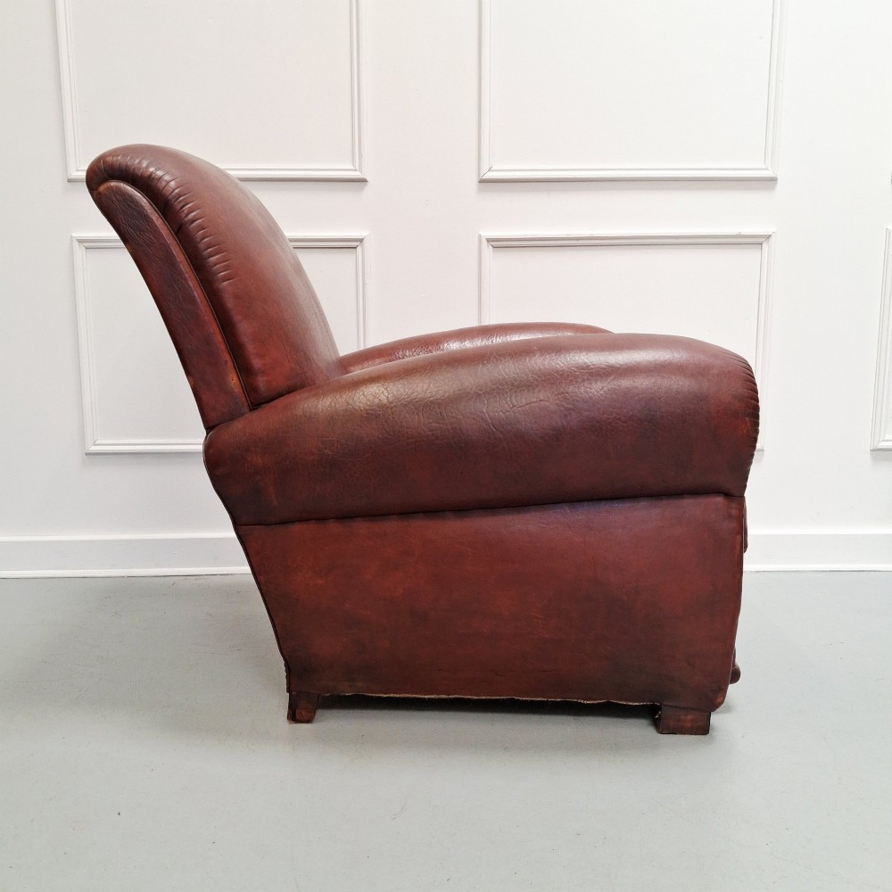 A French Art Deco club armchair upholstered in patinated brown leather with rolled arms, a high backrest, and low square feet. View II