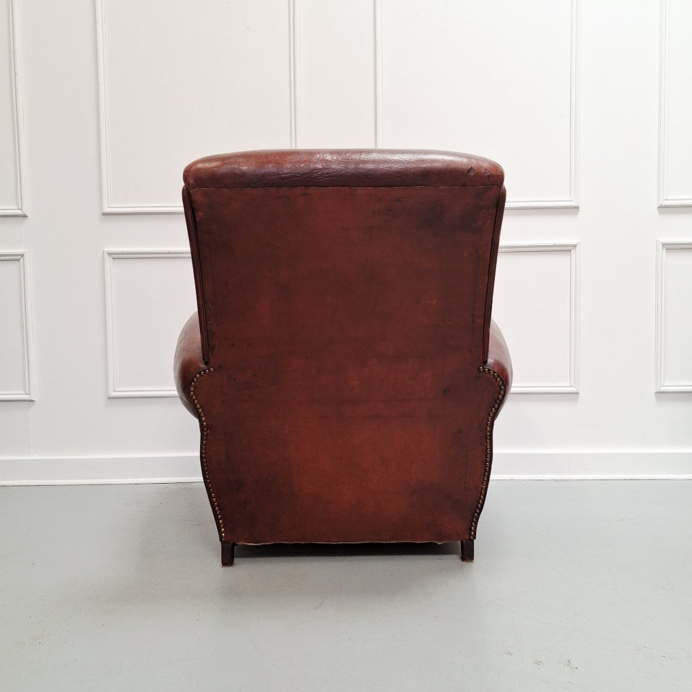 A French Art Deco club armchair upholstered in patinated brown leather with rolled arms, a high backrest, and low square feet. View III