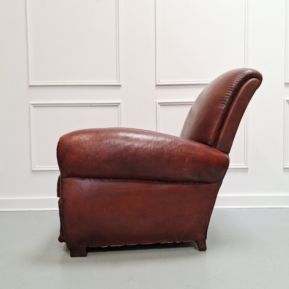 A French Art Deco club armchair upholstered in patinated brown leather with rolled arms, a high backrest, and low square feet. View IV