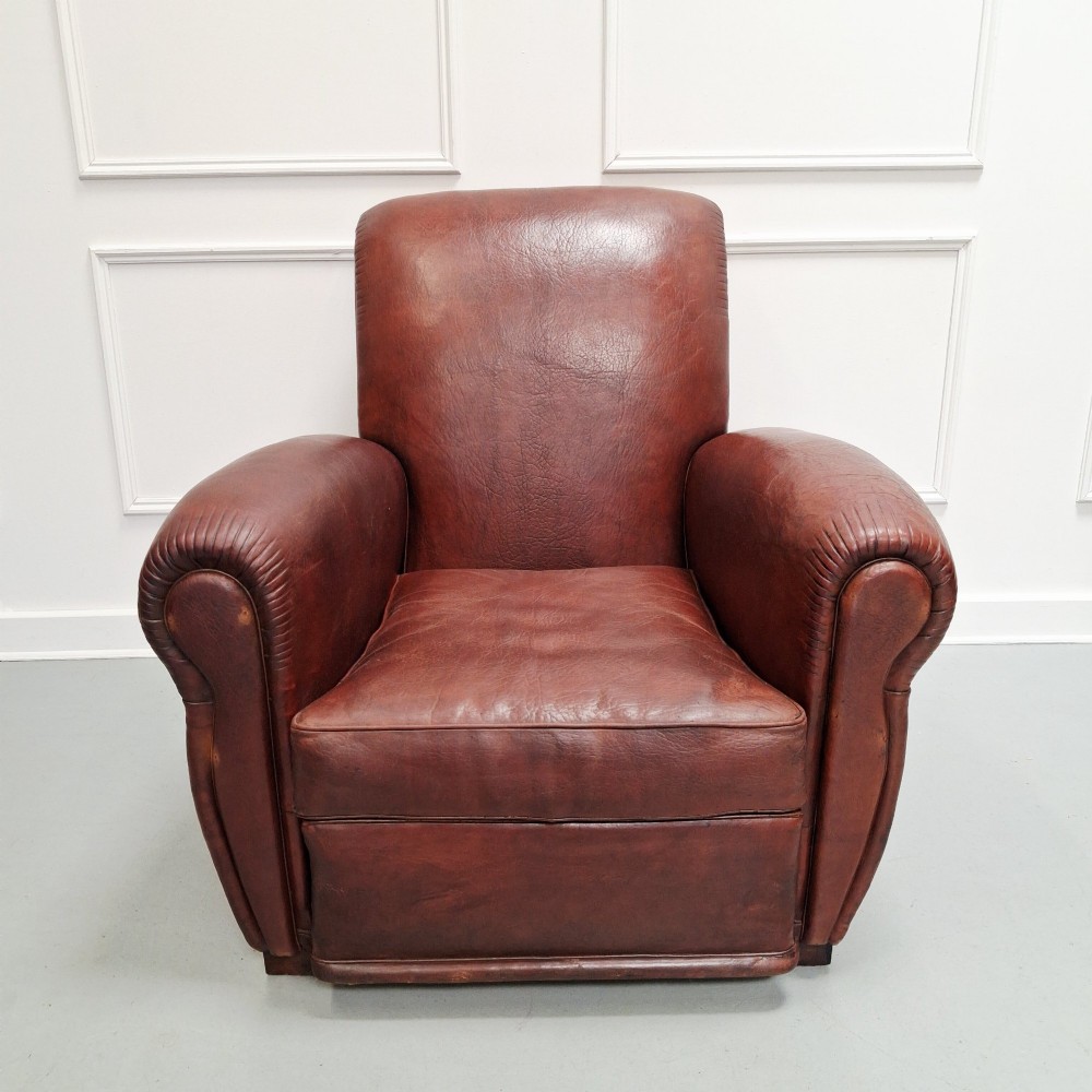 A French Art Deco club armchair upholstered in patinated brown leather with rolled arms, a high backrest, and low square feet. View V