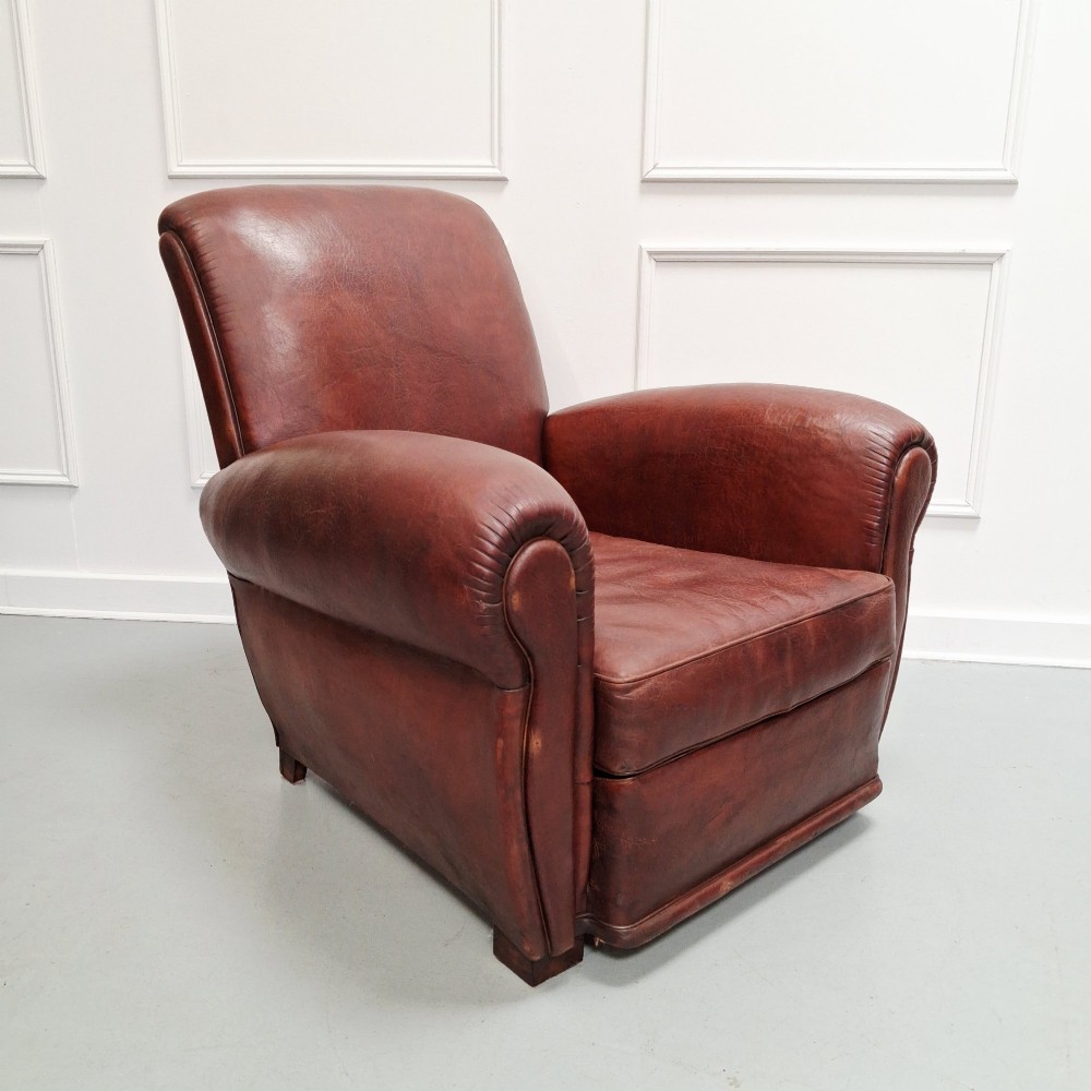 A French Art Deco club armchair upholstered in patinated brown leather with rolled arms, a high backrest, and low square feet. View VI