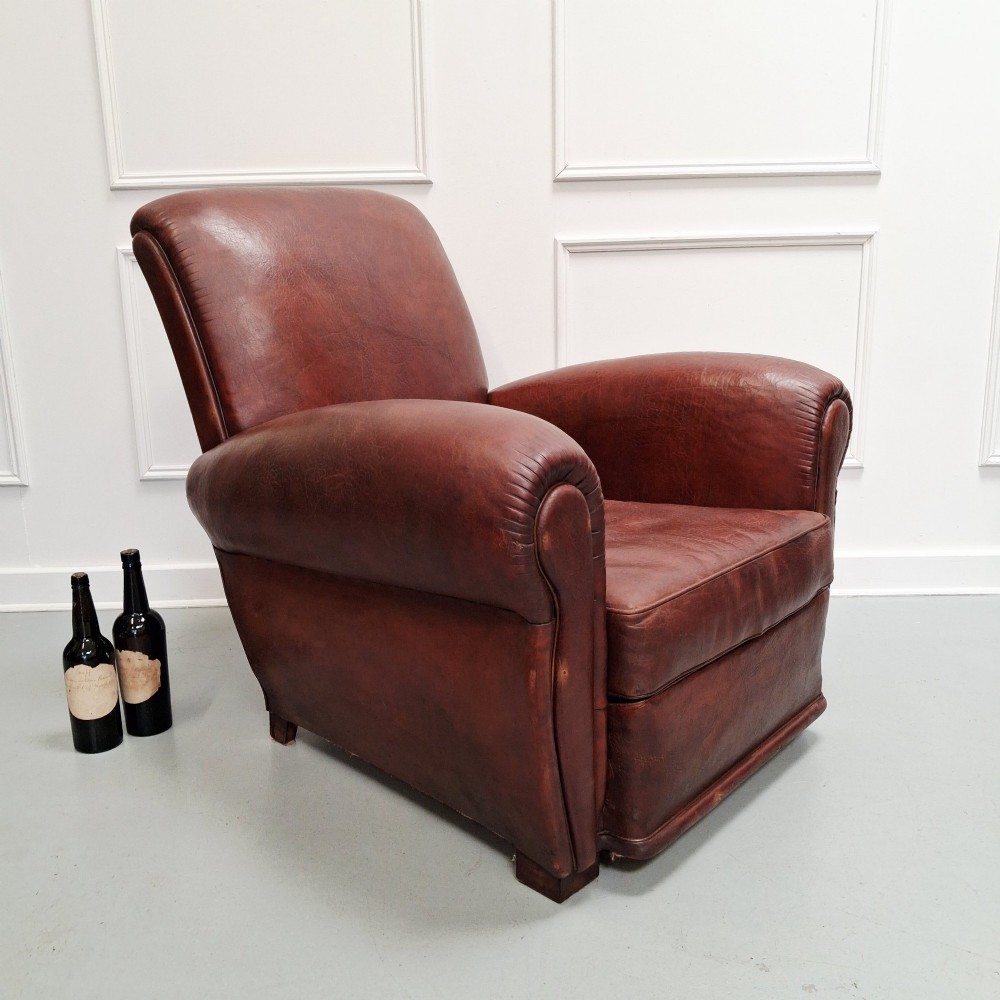 A French Art Deco club armchair upholstered in patinated brown leather with rolled arms, a high backrest, and low square feet. View VII