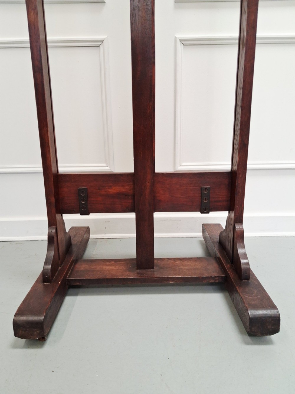 A tall dark oak studio easel featuring an adjustable central mast, upper clamp, solid lower shelf, and a heavy H-frame base. View VIII