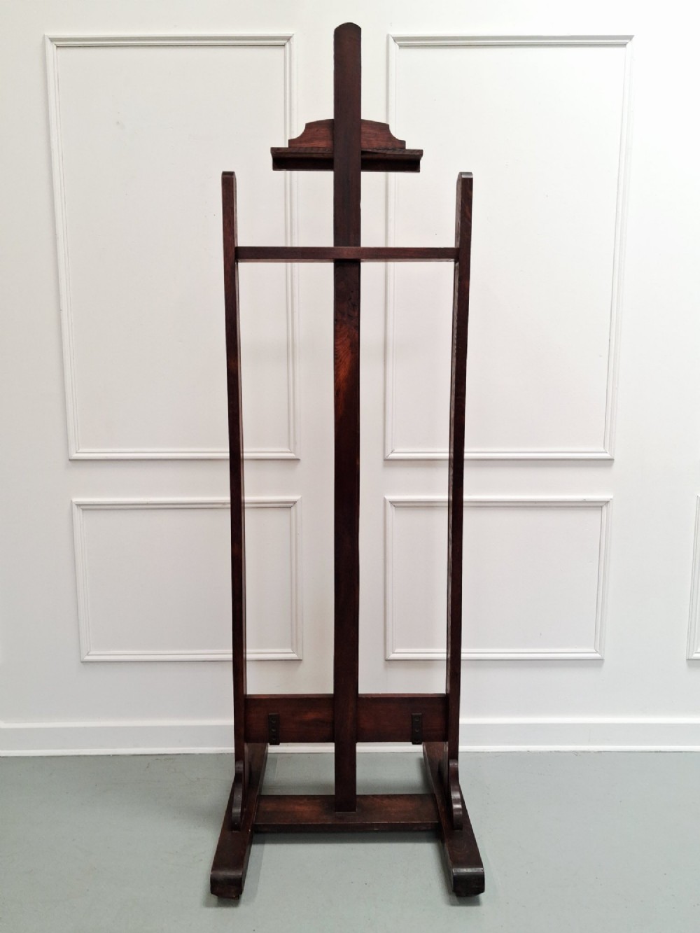 A tall dark oak studio easel featuring an adjustable central mast, upper clamp, solid lower shelf, and a heavy H-frame base. View IX