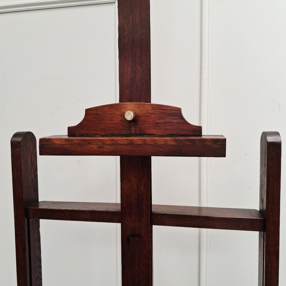 A tall dark oak studio easel featuring an adjustable central mast, upper clamp, solid lower shelf, and a heavy H-frame base. View XI