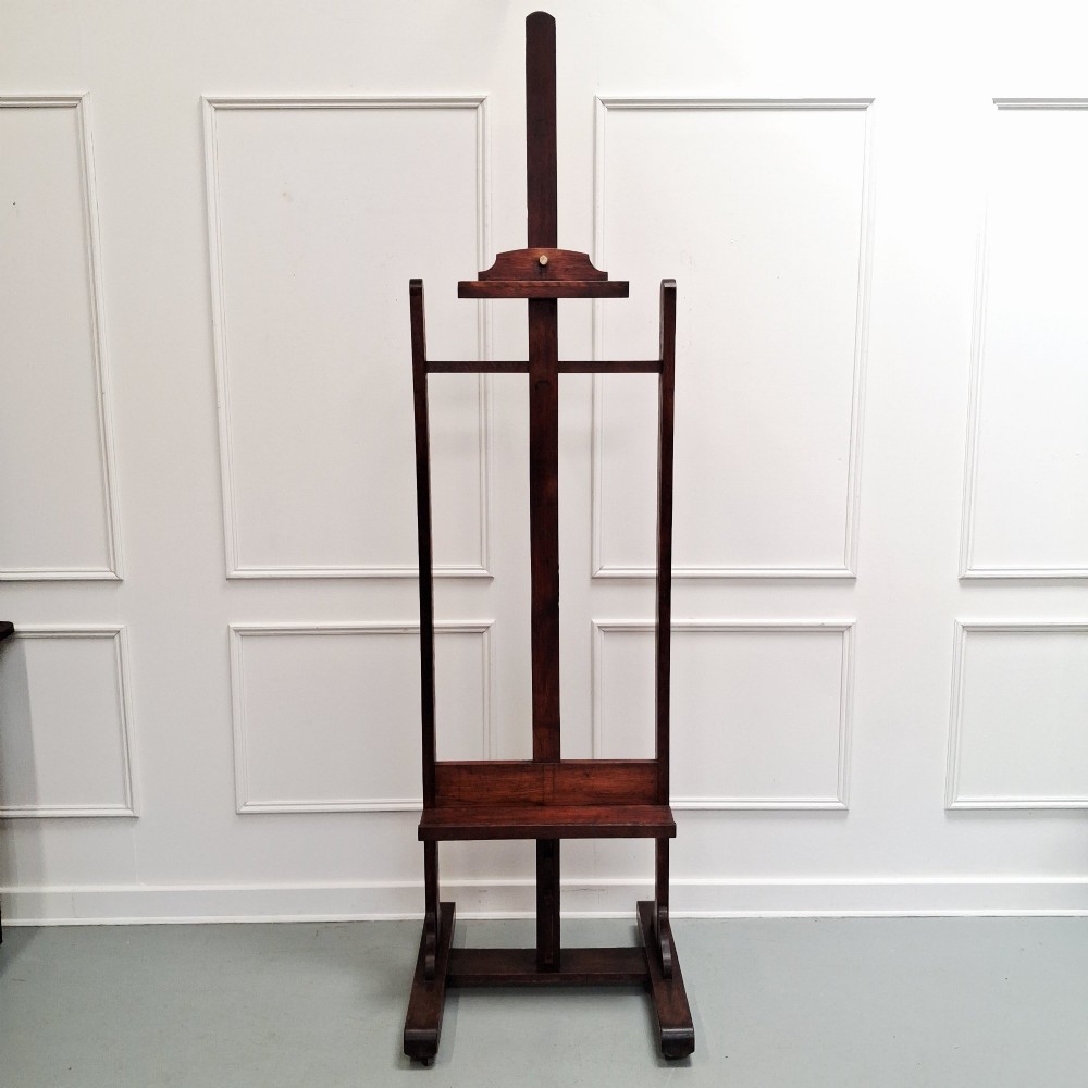 A tall dark oak studio easel featuring an adjustable central mast, upper clamp, solid lower shelf, and a heavy H-frame base. View XII