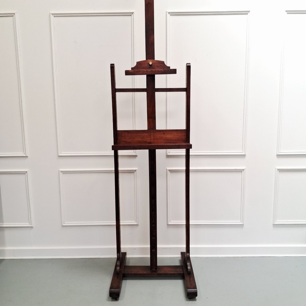 A tall dark oak studio easel featuring an adjustable central mast, upper clamp, solid lower shelf, and a heavy H-frame base. View XIII