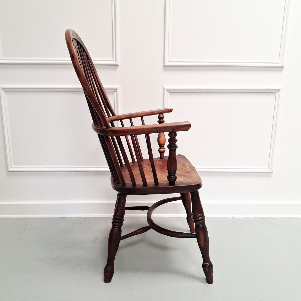 Side view of a mid-19th-century wooden Windsor armchair featuring turned front legs, spindle back, and shaped armrests.
