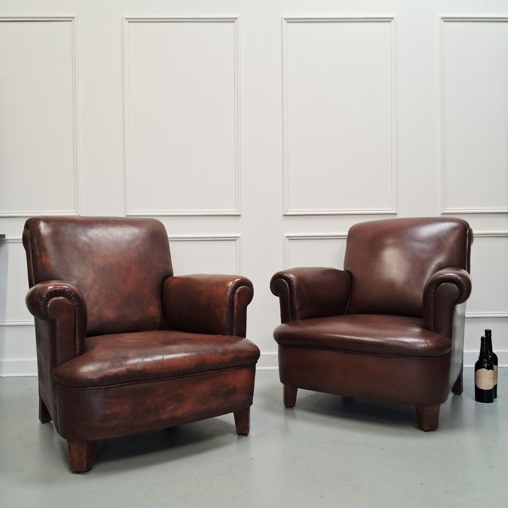 A pair of 1930s French club chairs upholstered in warm brown leather with rolled arms and short wooden feet. View V