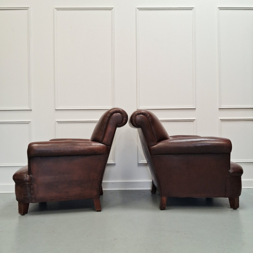A pair of 1930s French club chairs upholstered in warm brown leather with rolled arms and short wooden feet. View VII