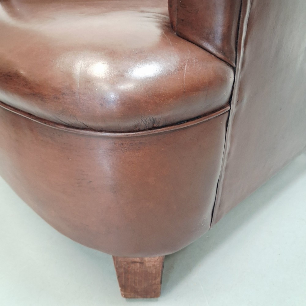 A pair of 1930s French club chairs upholstered in warm brown leather with rolled arms and short wooden feet. View X