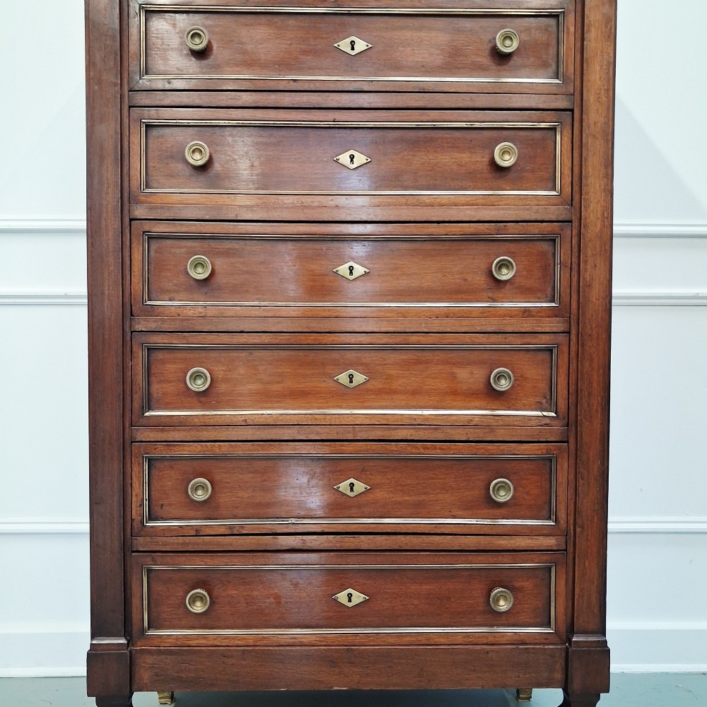 An antique French mahogany semainier tallboy featuring seven drawers with round brass pulls and diamond-shaped brass escutcheons set on short turned feet. View II