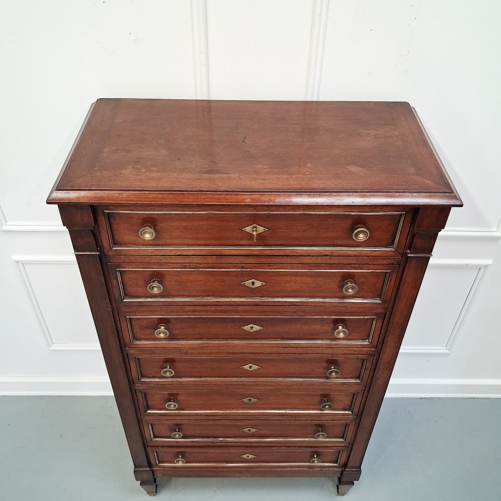 An antique French mahogany semainier tallboy featuring seven drawers with round brass pulls and diamond-shaped brass escutcheons set on short turned feet. View III