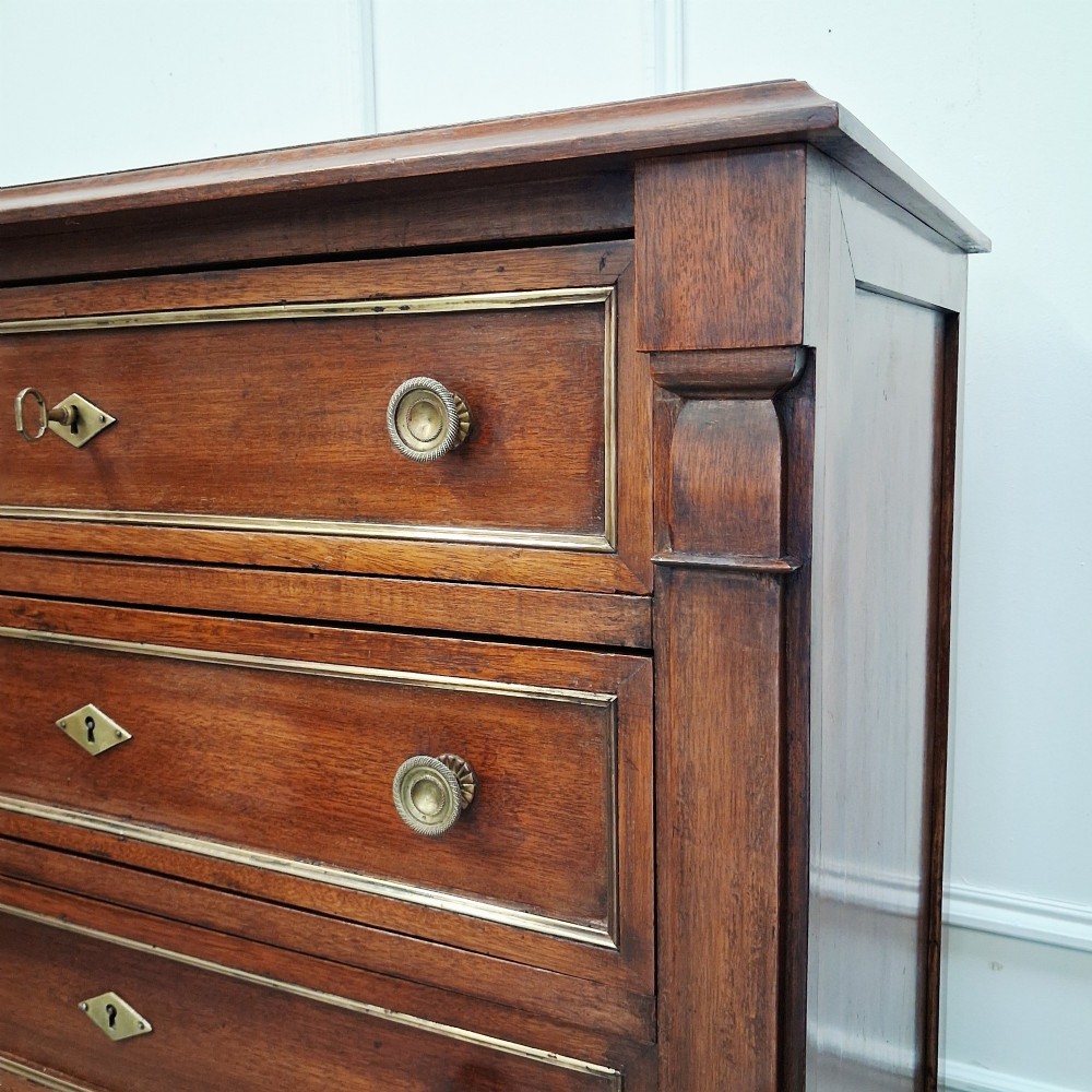 An antique French mahogany semainier tallboy featuring seven drawers with round brass pulls and diamond-shaped brass escutcheons set on short turned feet. View IV