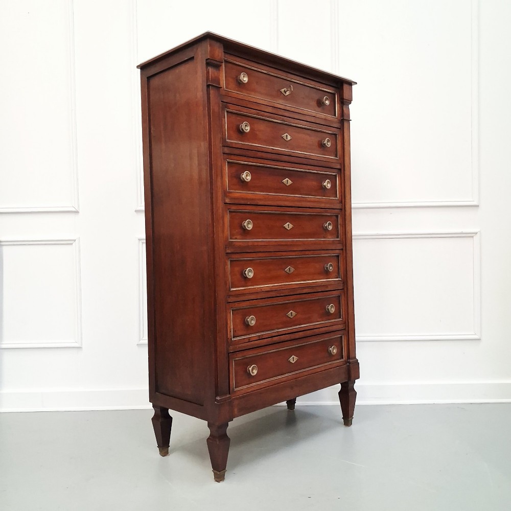 An antique French mahogany semainier tallboy featuring seven drawers with round brass pulls and diamond-shaped brass escutcheons set on short turned feet. View VIII