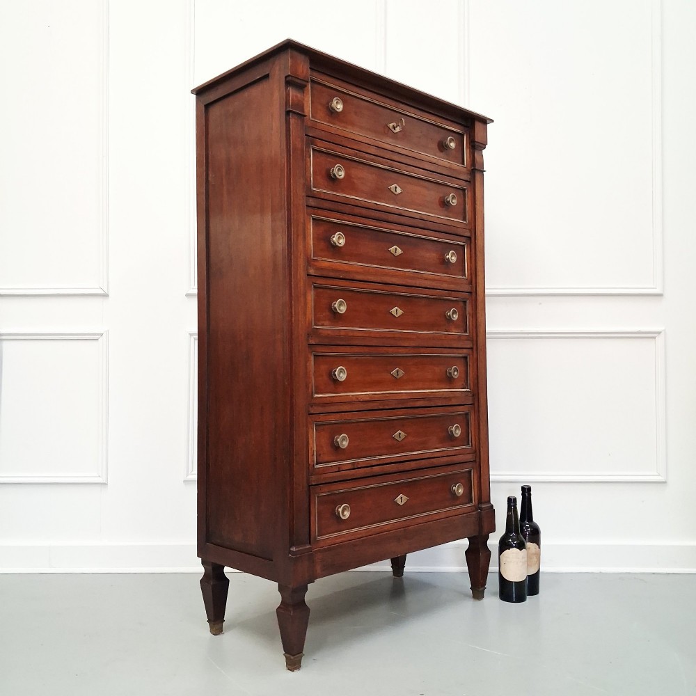 An antique French mahogany semainier tallboy featuring seven drawers with round brass pulls and diamond-shaped brass escutcheons set on short turned feet. View IX