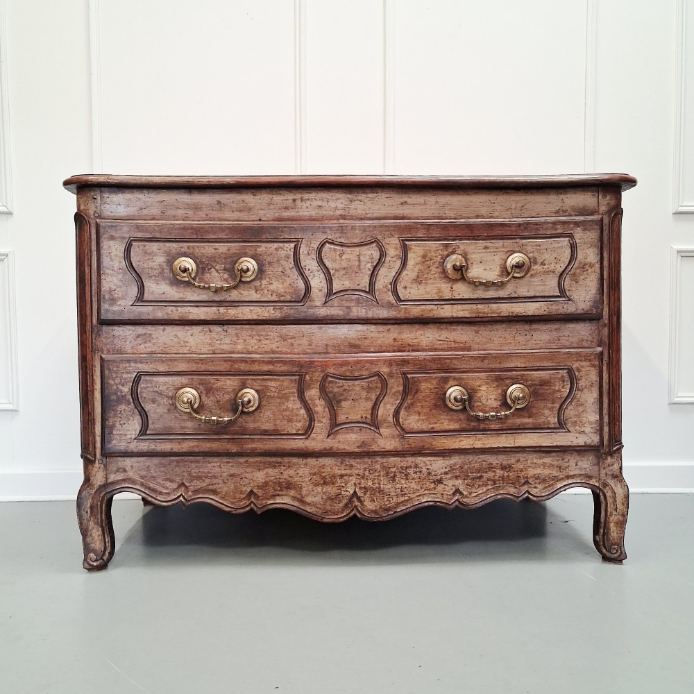 An antique French oak commode featuring two wide drawers with carved moulded panel details, brass drop handles, a scalloped lower apron, and short cabriole feet.
